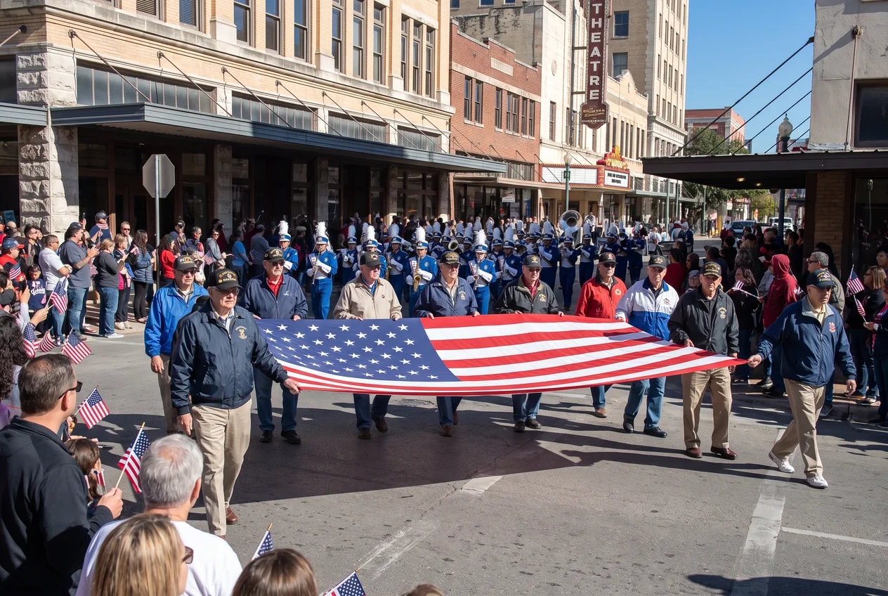 Veterans in unit ball caps marching down Houston Street in downtown San Antonio on a bright November day, spectators with small American flags lining the kerb in front of historic brick storefronts